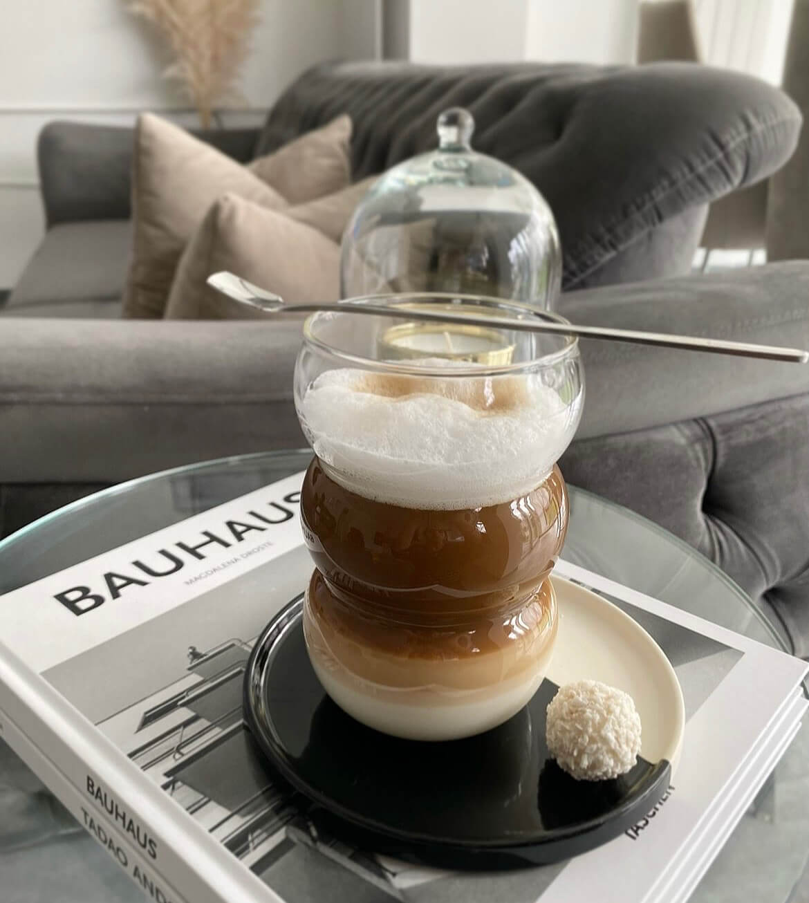 Cappuccino serviert in einem modernen Bubble Glas | Ibiza Sunkissed auf einem Buch mit einem Untersetzer - Luxuriöse, ästhetische Glasware für erfrischende und heiße Getränke.