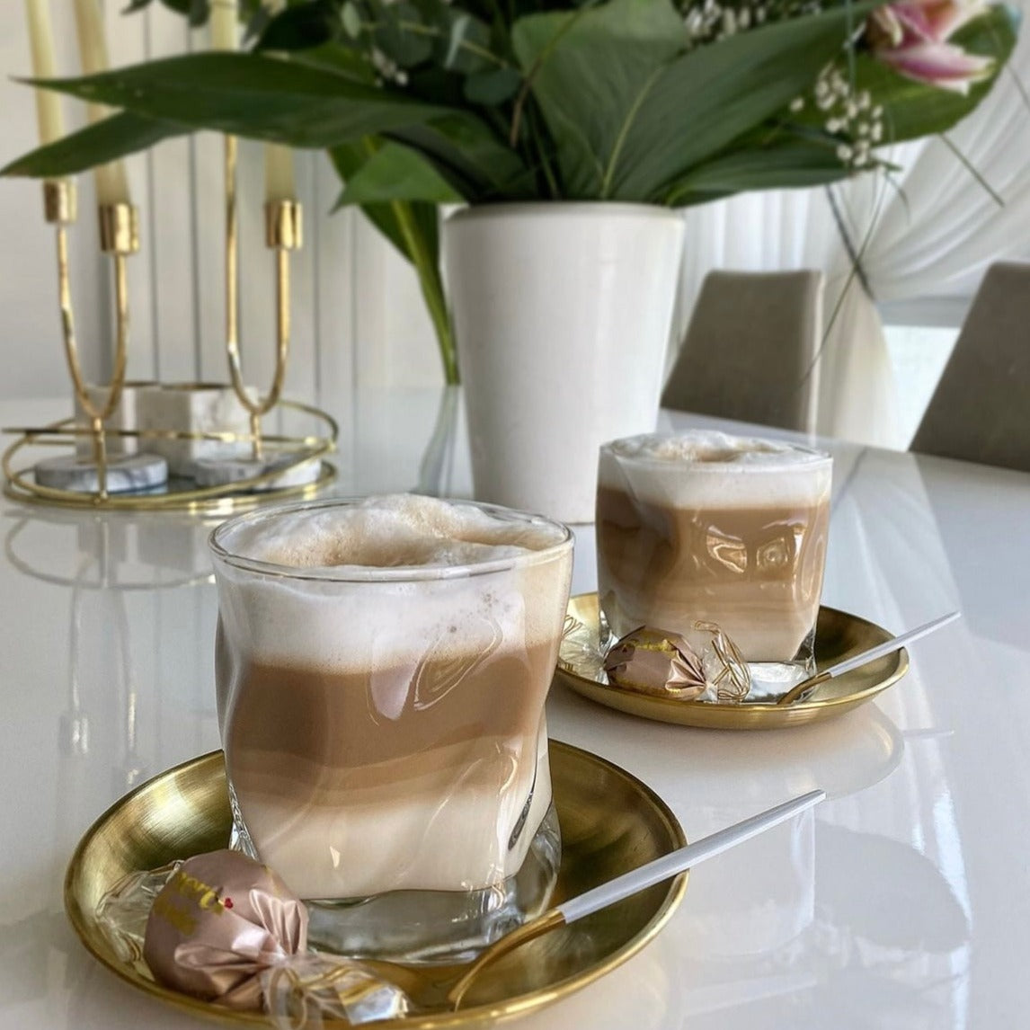 Ein stilvolles und ästhetisches Diamond Twist Glas, präsentiert auf einem Tisch mit köstlichem Cappuccino darin. Die Gläser stehen auf Untertassen mit Schokolade. Luxuriöses Trinkglas mit markantem Design und ästhetischem Appeal. Perfekt für Cocktails, Whiskey oder erfrischende Getränke. Erleben Sie Luxus und Eleganz mit diesem hochwertigen, einzigartigen Glas. Ideal für den täglichen Gebrauch oder besondere Anlässe. Stilvoll und zeitlos gestaltet für anspruchsvolle Genießer.