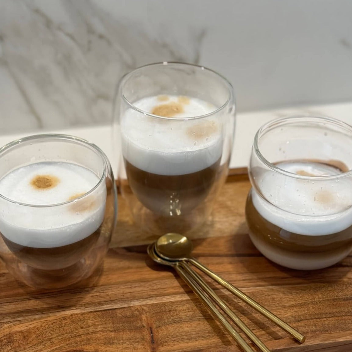 Unser Double Wall Glas 250ml mit doppelwandigem Design, gefüllt mit Cappuccino, auf einem Tisch. Dieses modern und minimalistisch designte Trinkglas ist hochwertig, stilvoll und bietet ein einzigartiges Trinkgefühl. Perfekt für kalte und heiße Getränke, wie Kaffee und Cappuccino. Ein attraktiver und edler Blickfang, der Luxus und Eleganz ausstrahlt.