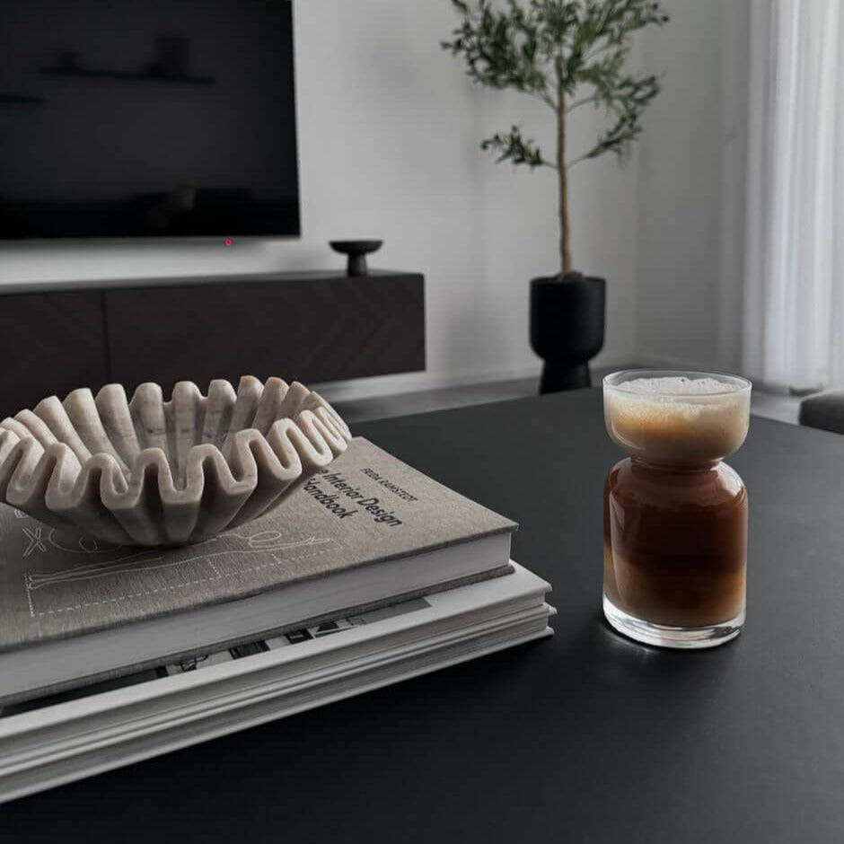 Unser London Sandscape Glas mit Sanduhr-Design, gefüllt mit Eiskaffee, auf einem Tisch. Dieses stilvolle, modern und minimalistisch designte Trinkglas ist hochwertig, elegant und bietet ein einzigartiges Trinkgefühl. Perfekt für kalte und heiße Getränke, wie Kaffee und Eiskaffee. Ein attraktiver und edler Blickfang, der Luxus und Ästhetik ausstrahlt.