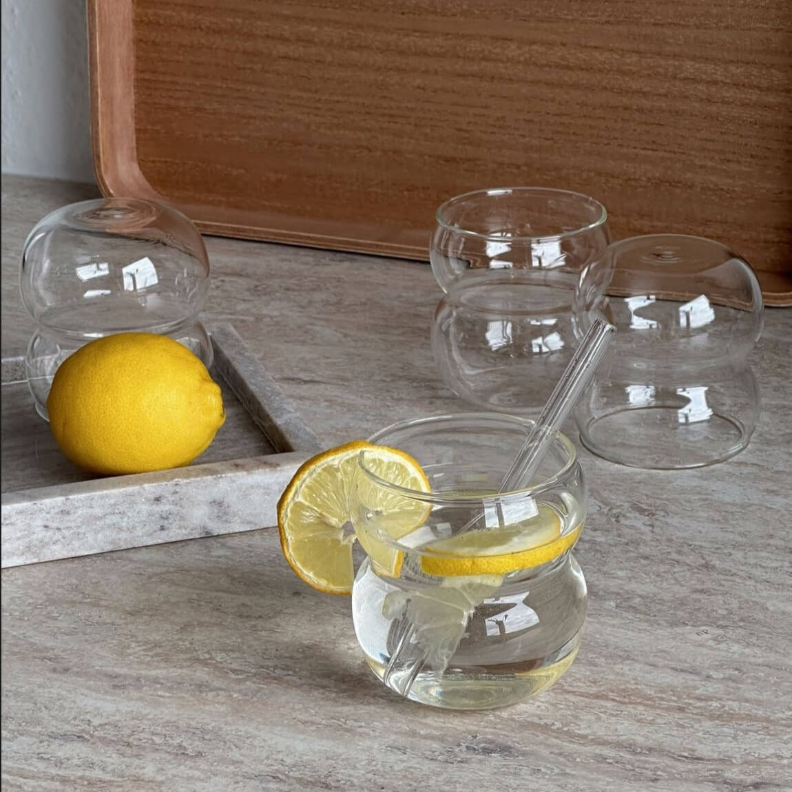 Unser stilvolles Bubble Glas | Parisian Love, gefüllt mit erfrischendem Wasser und Zitronenscheiben. Dieses hochwertige Trinkglas mit wellig gewölbtem Bubble-Design ist ideal für kalte und heiße Getränke. Perfekt für elegante, moderne und minimalistische Tischdekorationen. Genießen Sie Luxus und Ästhetik bei jedem Schluck. Ein einzigartiges, edles Glas für ein besonderes Trinkgefühl und ein attraktiver Blickfang in jeder Umgebung.